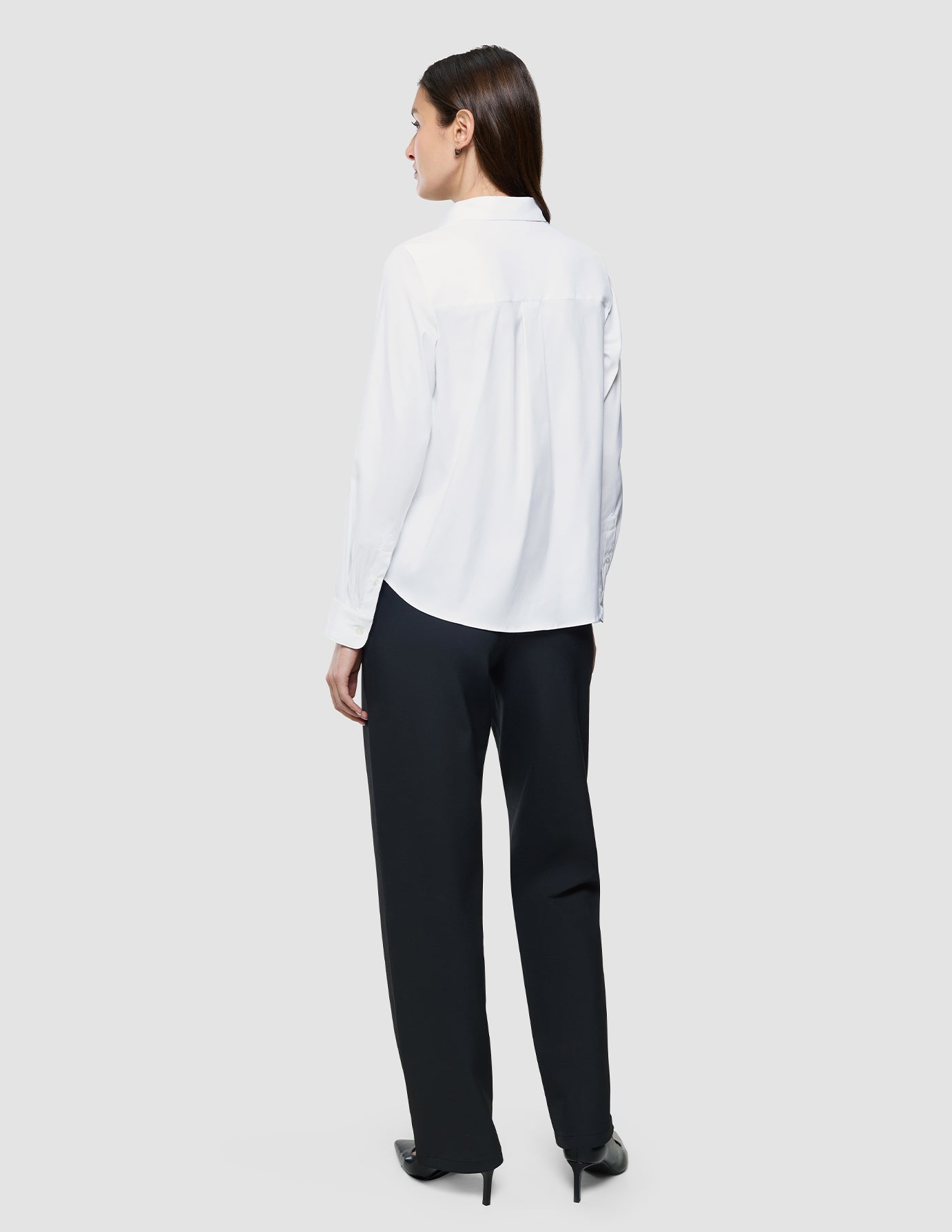 En kvinne sett bakfra, kledd i en hvit «Women Oxford Shirt» i vanlig passform og svarte bukser med skandinavisk design.